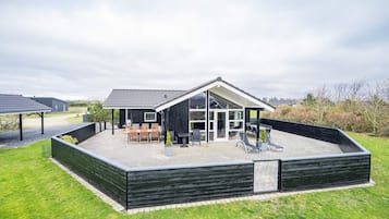 Una casa moderna con un porche cubierto, mobiliario exterior y vistas del paisaje circundante.