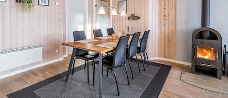 Un interior moderno con un revestimiento de madera, una mesa de comedor con sillas, una chimenea y una planta colgante.