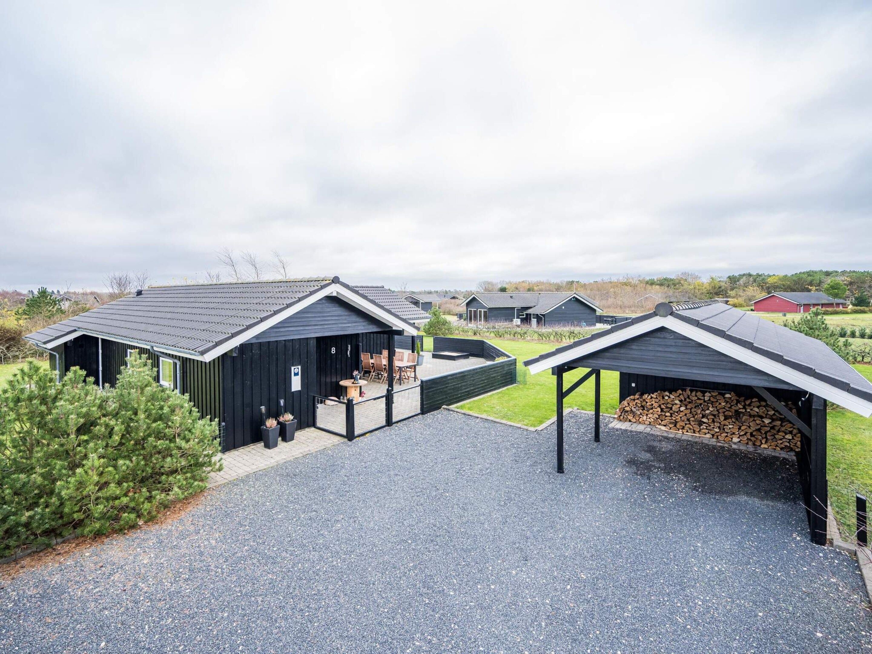 A modern building with a covered outdoor seating area and a stack of firewood.