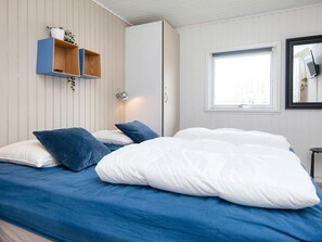 A bedroom with a bed, pillows, a wardrobe, a shelf with plants, and a window. - Holiday Home in FanÃ¸ (Fano)