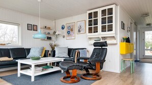 A modern living room with a black leather sofa, a white coffee table, and a black leather chair with wooden legs. There is a white cabinet with glass doors and a yellow shelf. - Holiday Home in FanÃ¸ (Fano)