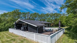 A cabin with a deck, surrounded by a white fence, set in a wooded area. - Holiday Home in FanÃ¸ (Fano)
