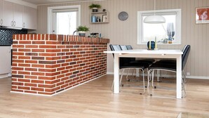A modern kitchen with a brick island, white cabinets, and a dining area with a white table and black chairs. - Holiday Home in FanÃ¸ (Fano)