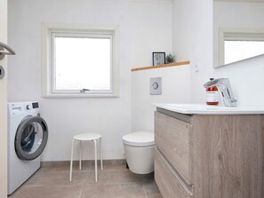 A compact bathroom with a washing machine, a toilet, and a sink with a mirror. - Holiday Home in FanÃ¸ (Fano)