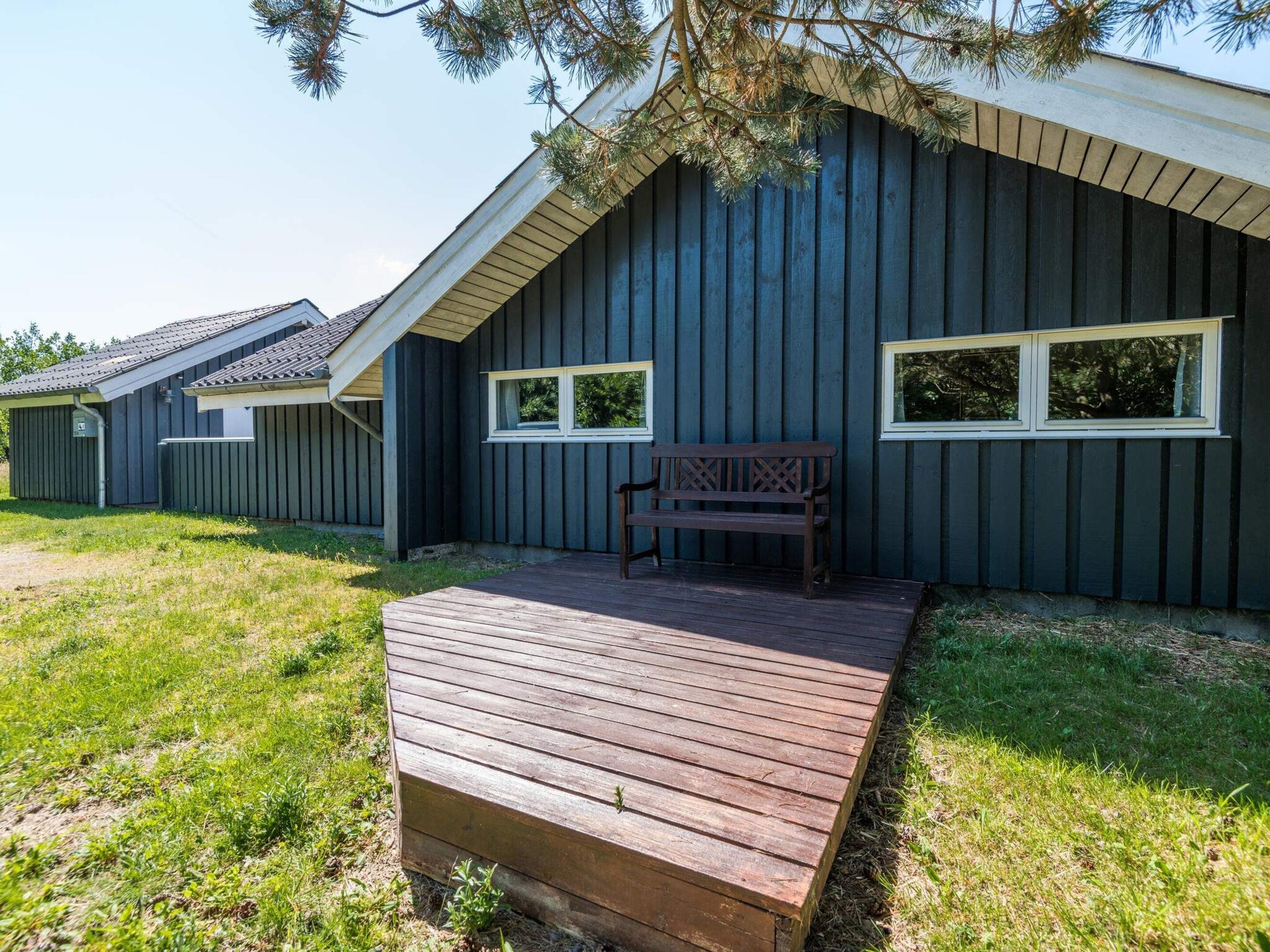 A building with a dark exterior, a wooden deck, and a bench.