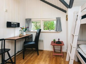 Una habitación con literas, un escritorio con silla, una mesita con una planta en maceta, un microondas y una ventana con cortinas.