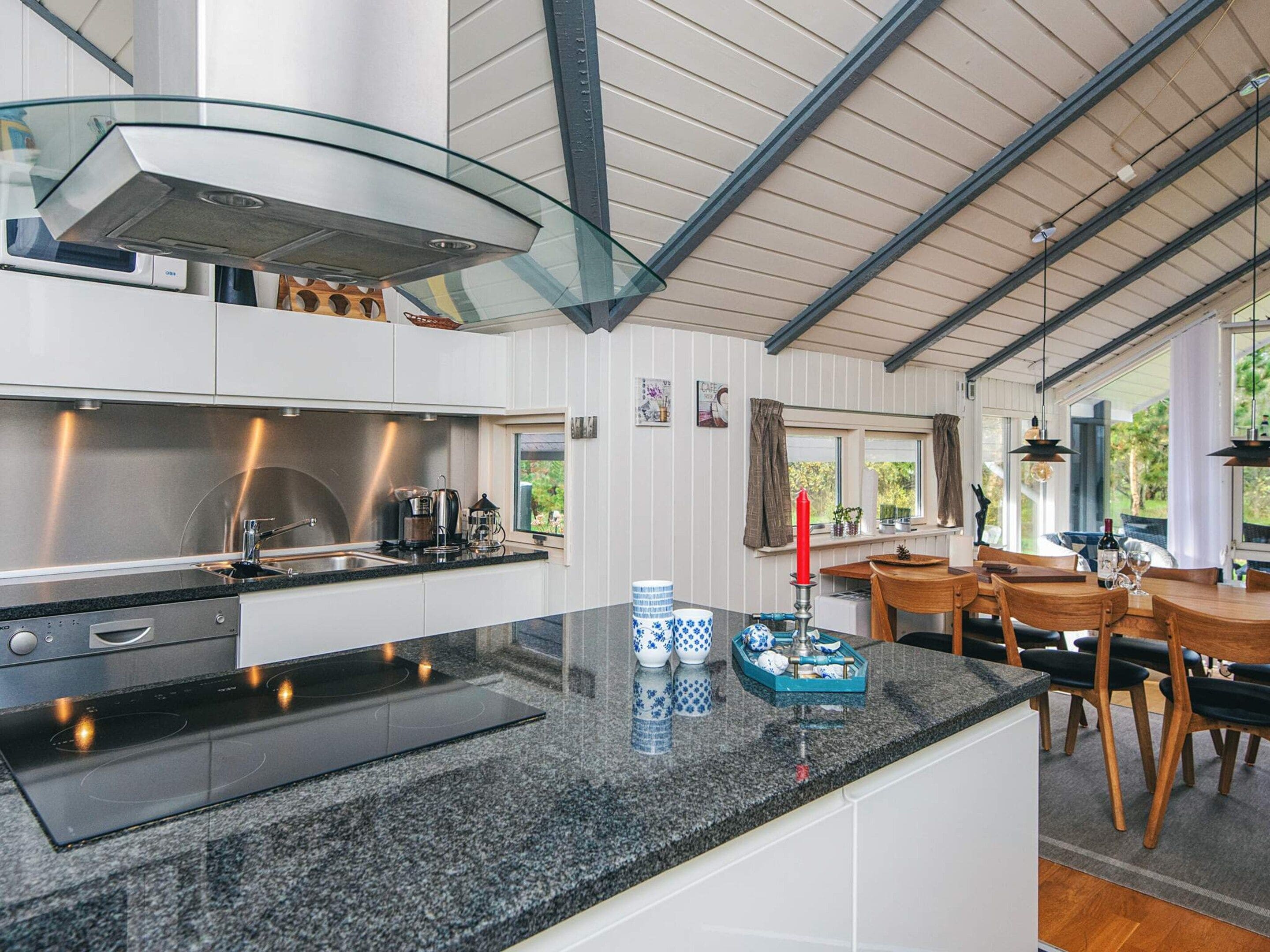 A modern kitchen with a central island, stainless steel appliances, and a dining area with wooden furniture.