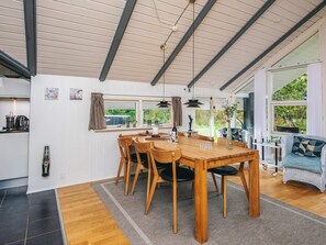 Un comedor con una mesa y sillas de madera, una zona de cocina con cafetera, y vistas a zonas verdes exteriores.