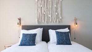 Ein Doppelbett mit weißen und blauen Kissen, ein dunkles Kopfteil und ein Wandbehang aus Makramee.