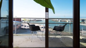 Ein Balkon mit zwei Stühlen und einem großen Blatt. Im Blickfeld befindet sich ein Gewässer und eine Anlegestelle mit Booten.
