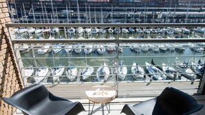 Ein Balkon mit zwei schwarzen Stühlen und einem kleinen runden Tisch, mit Blick auf einen Yachthafen und zahlreichen dort liegenden Booten.