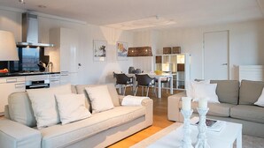 A modern living room with a sofa, a dining table, and a kitchen area. - Apartment in Scheveningen With Harbor View (The Hague)