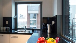 A modern kitchen with a large window, a bowl of fruit on the counter, and a view of a building outside. - Apartment in Scheveningen With Harbor View (The Hague)