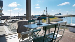 A balcony with a table and chairs, overlooking a body of water and a bridge. - Apartment in Scheveningen Near the Harbor (The Hague)