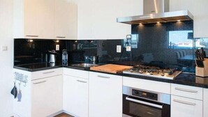 A modern kitchen with white cabinets, black countertops, a stainless steel range hood, and a built-in oven. - Apartment in Scheveningen Near the Harbor (The Hague)