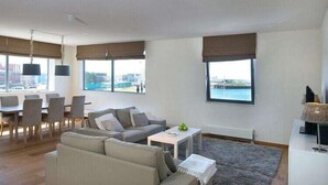 A modern living room with a sofa, a coffee table, and a dining area with chairs. - Apartment in Scheveningen Near the Harbor (The Hague)