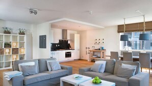 A modern living room with two grey sofas, a coffee table, and a dining area with a table and chairs. - Apartment in Scheveningen Near the Harbor (The Hague)