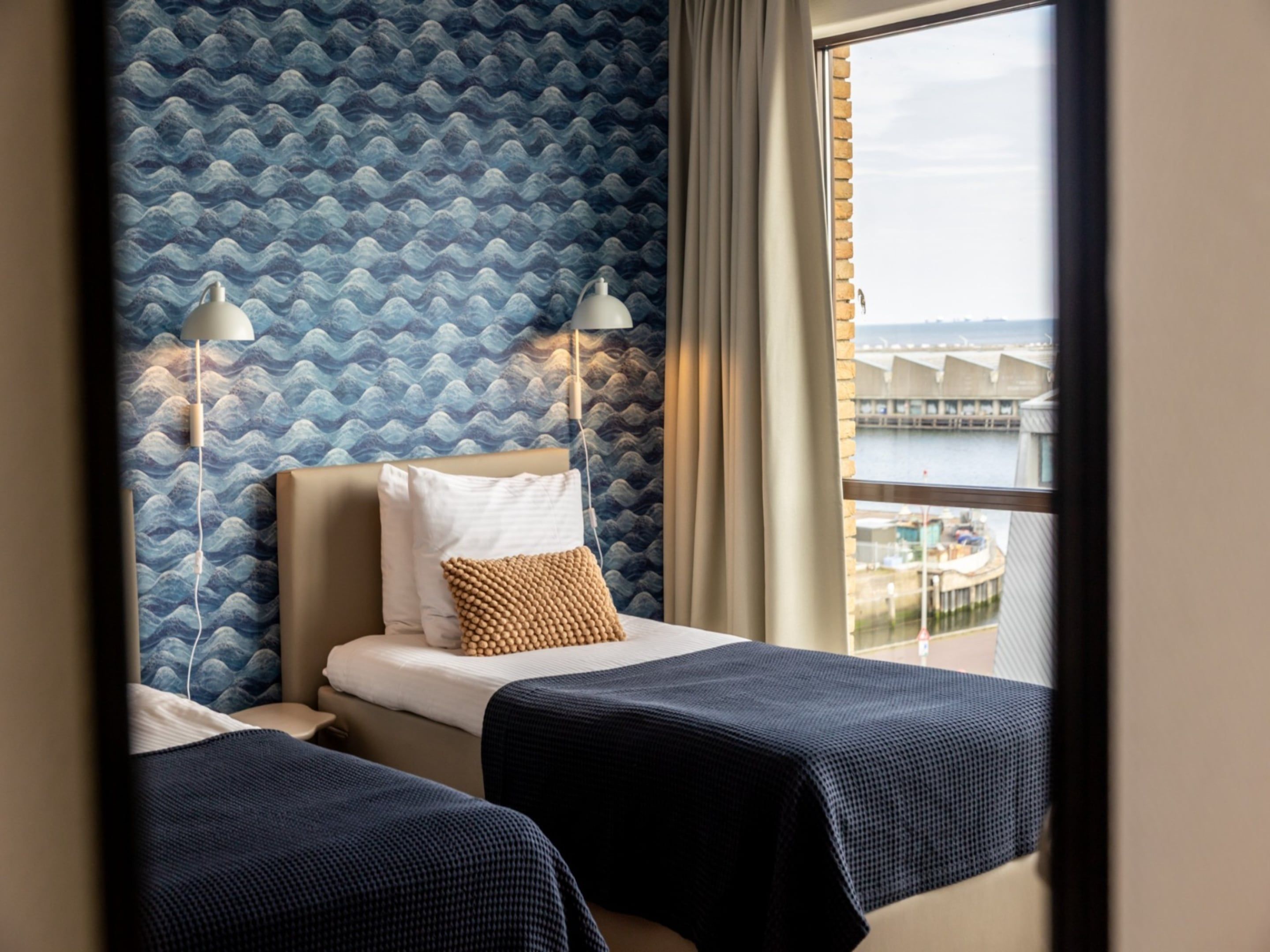Habitación de hotel con dos camas, vista a un cuerpo de agua y pared con diseño.