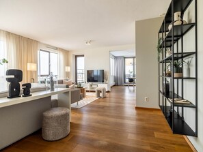 Egy modern nappali, melyben található egy síkképernyős televízió, egy kanapé, egy dohányasztal és egy könyvespolc.