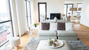 A modern living room with a large window, a flat-screen TV, and a dining area with chairs and a table. - Luxury Apartment With a View (The Hague)