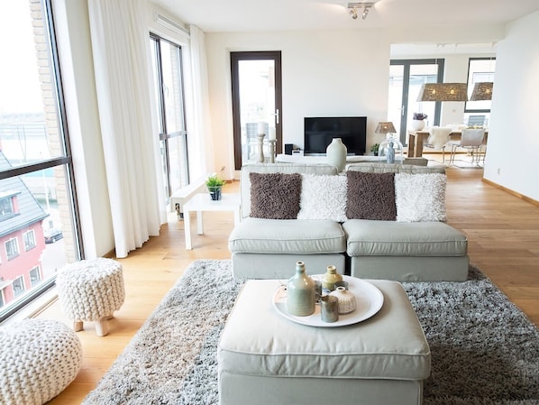 A modern living room with a large window, a flat-screen TV, and a dining area with chairs and a table. - Luxury Apartment With a View (The Hague)