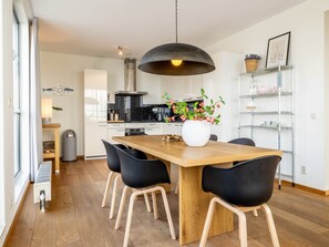 A modern kitchen with a wooden dining table, black chairs, a hanging light fixture, and a potted plant. - Luxury Apartment With a View (The Hague)