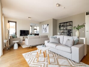 A modern living room with a sofa, a coffee table, and a TV. - Luxury Apartment With a View (The Hague)