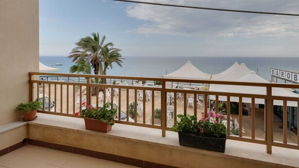 A balcony with a view of the sea, white umbrellas, and potted plants.