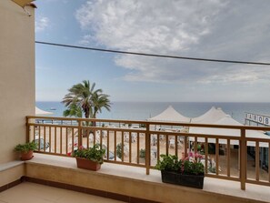 Un balcón con vista al mar, sombrillas blancas y plantas en macetas.