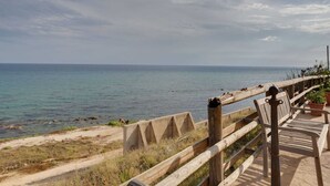 A coastal walkway with a wooden railing, a concrete barrier, and a bench.