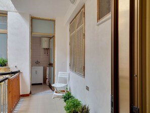 A narrow corridor with a white chair, a potted plant, and a door leading to a kitchen area.