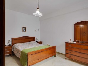 A bedroom with a wooden bed, a nightstand, a dresser, and a hanging light fixture.