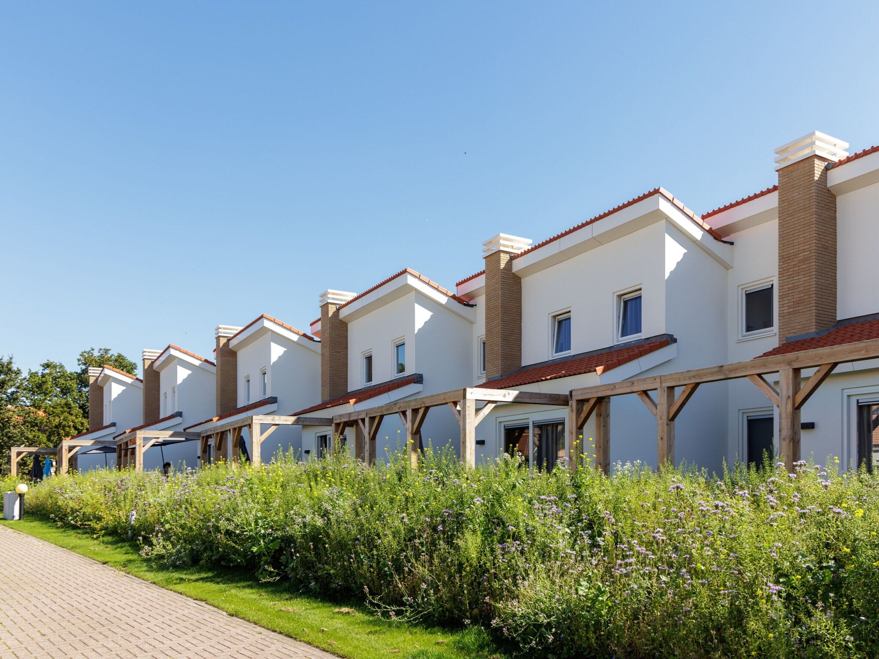 A row of modern townhouses with brick chimneys, wooden balconies, and a well-maintained garden in front.