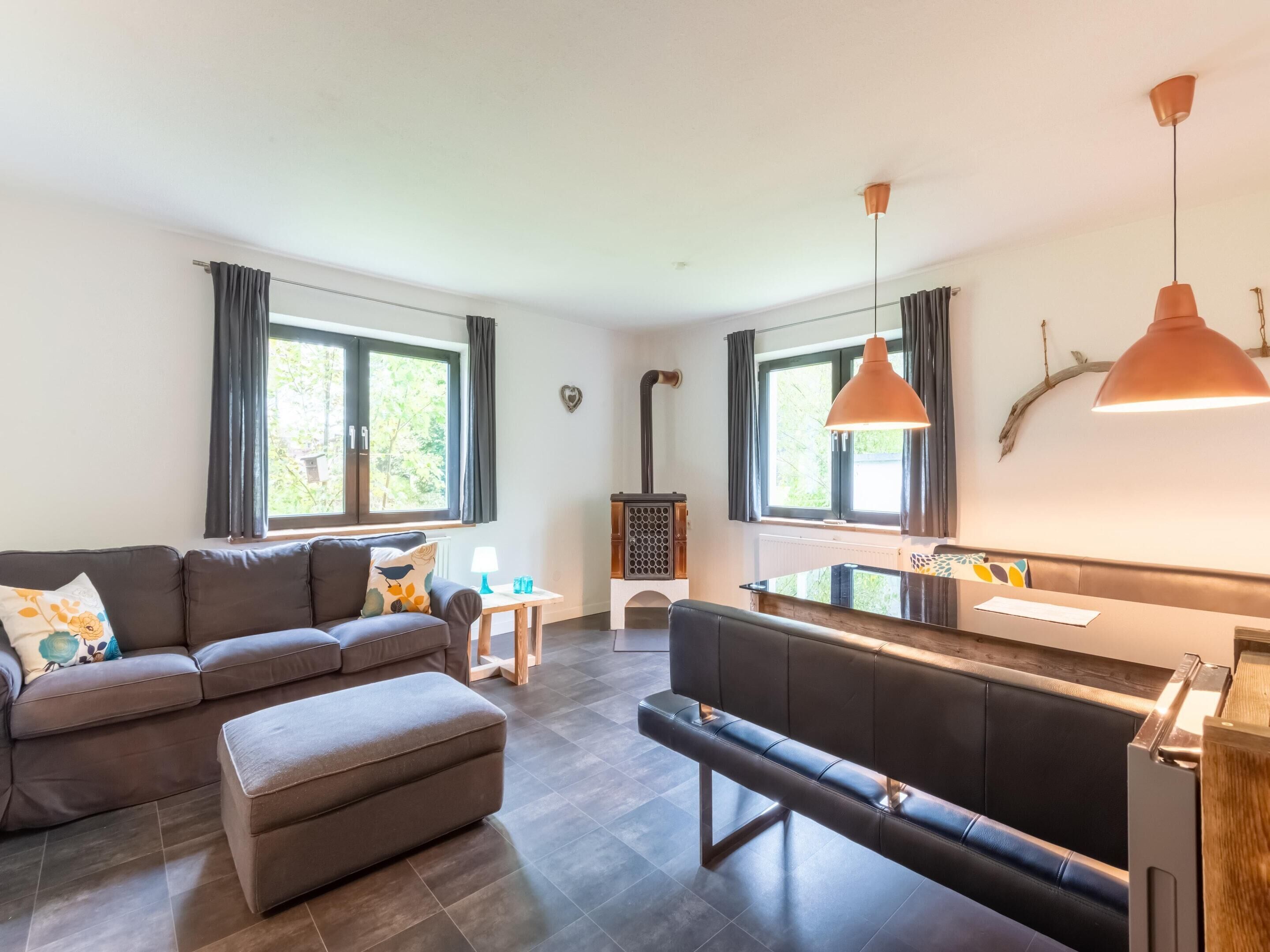A modern living room with a sofa, ottoman, and bench, a small table with a lamp, and a kitchen area with a stove.