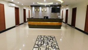 Un espace d’accueil d’hôtel comprenant un comptoir de réception, une horloge et un téléviseur à écran plat fixé au mur.