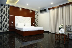 A modern hotel room with a large bed, a glass coffee table, a sofa, and a decorative vase. - Ilva Hotel (Lahore)