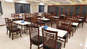 Un grand espace dédié à la salle à manger, avec de nombreuses tables et chaises, des climatiseurs fixés aux murs et de grandes fenêtres.