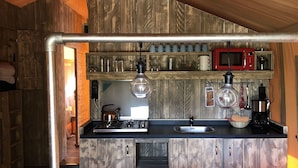 A rustic kitchen with wooden walls, a gas stove, a sink, a microwave, and various kitchen utensils.