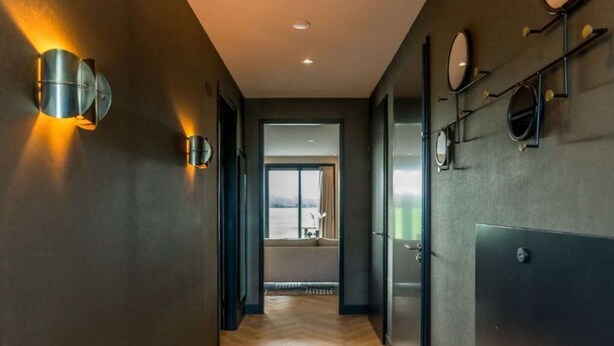 A hallway with wooden flooring, dark walls, and wall-mounted lighting fixtures. - Luxury Villa on Texel Near Sandy Beaches (De Cocksdorp)
