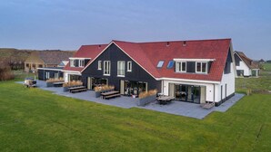 Une maison moderne avec un toit rouge, de grandes fenêtres et un vaste espace patio.