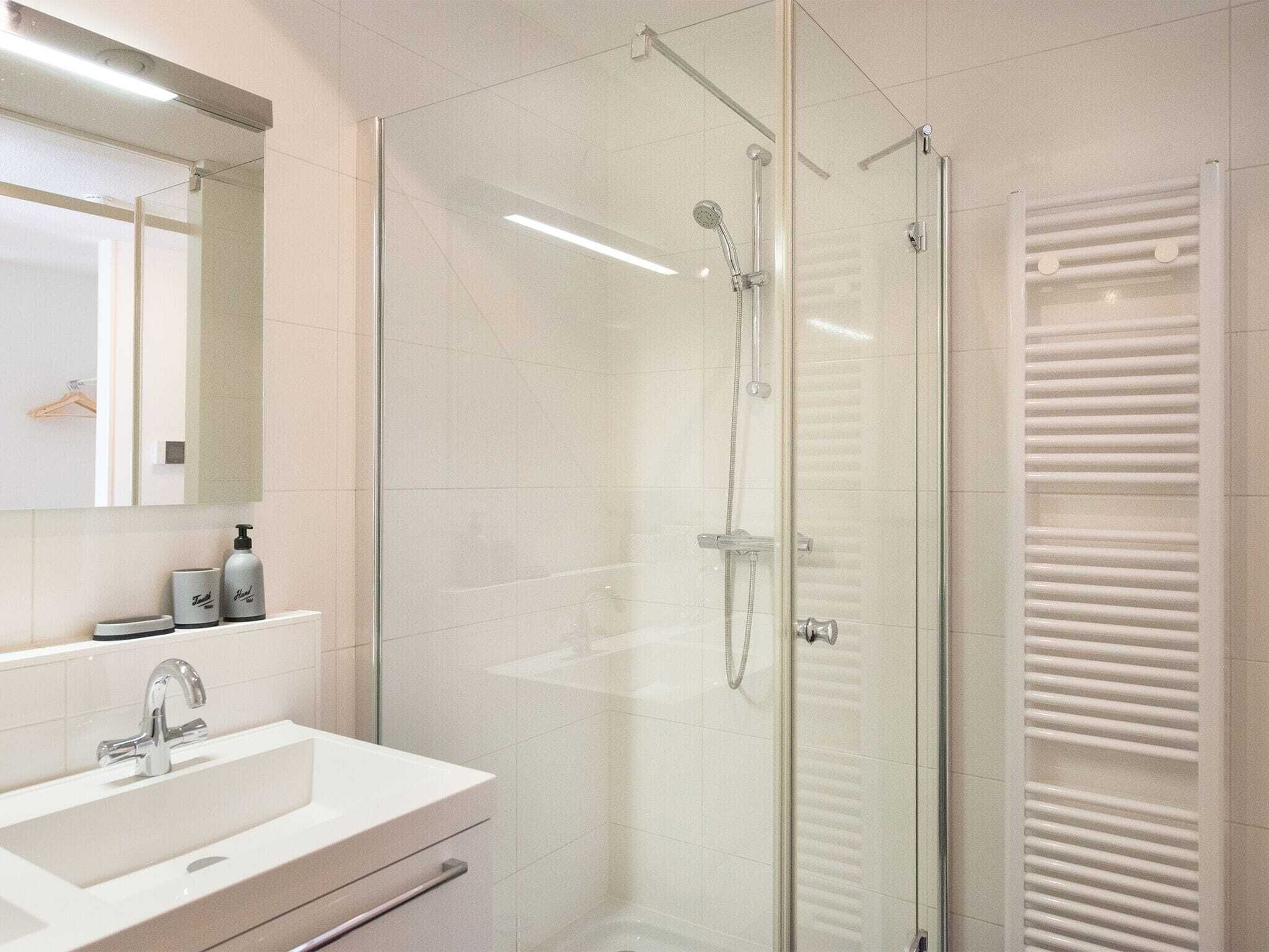 Ein modernes Badezimmer mit einer Duschkabine aus Glas, einem weißen Waschbecken und einem Spiegel darüber.