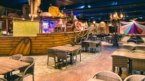 Restaurante com tema náutico, com mesas de madeira e cadeiras de vime, um leme de navio e um salva-vidas.