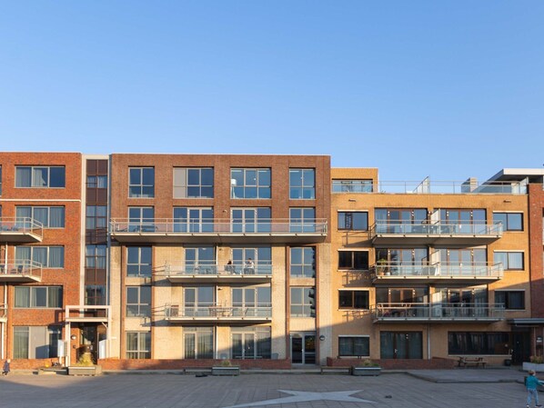 Un immeuble à plusieurs étages, doté d’une façade en briques, de nombreux balcons et surplombant un ciel dégagé.