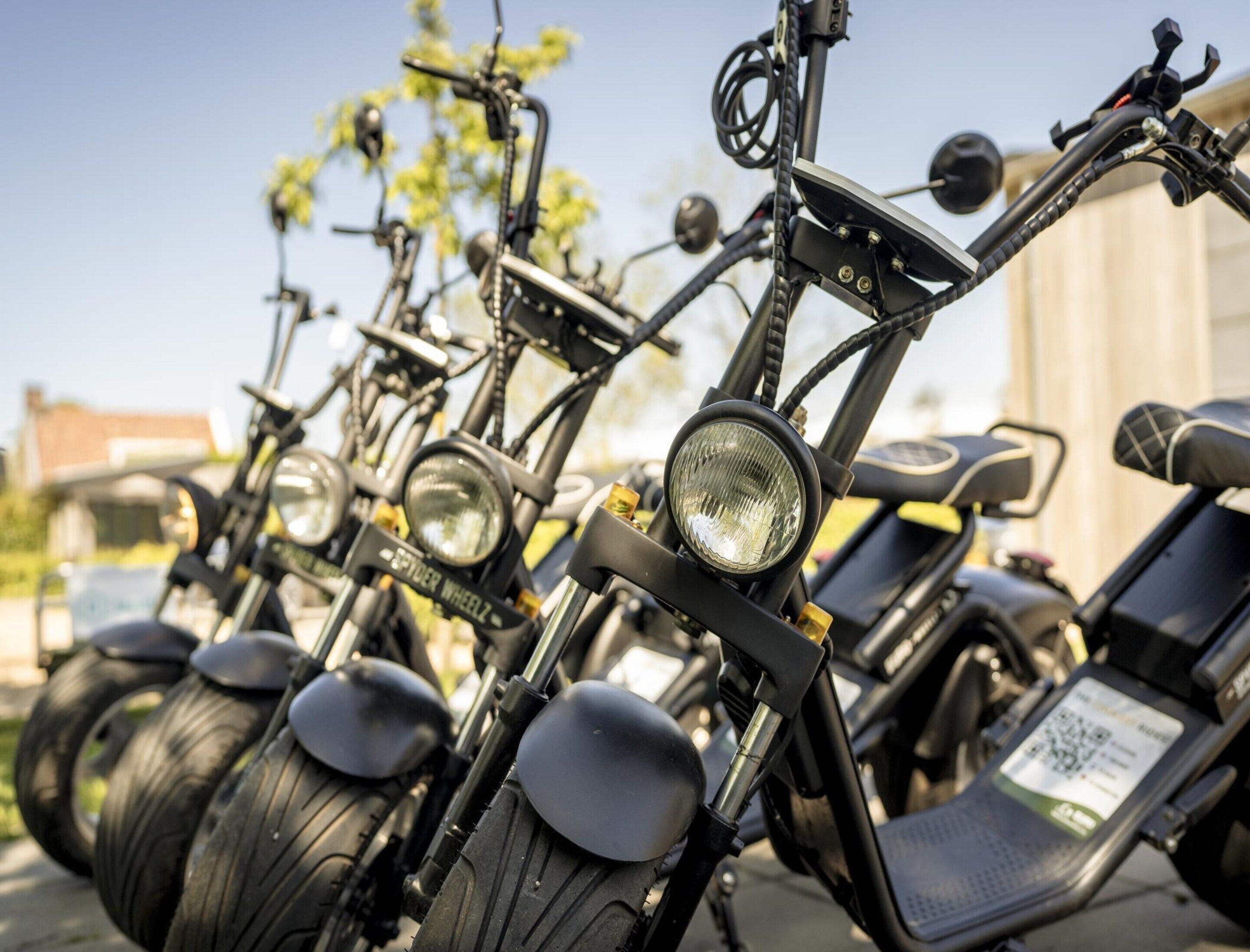 Uma fileira de bicicletas elétricas estacionadas ao ar livre, com guidões, rodas e um código QR visível no selim.