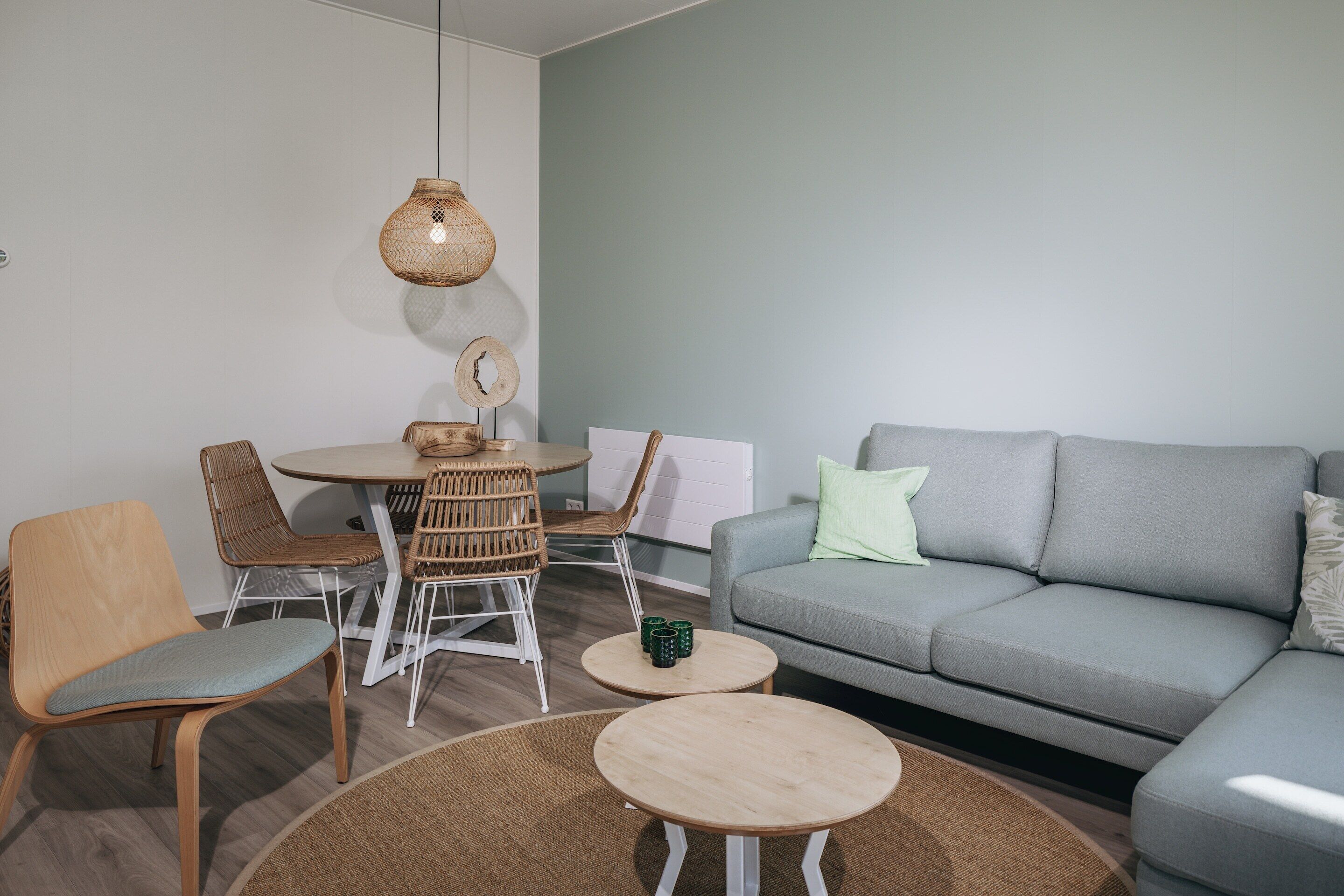 A living room with a grey sofa, wooden chairs, a round table, and a hanging light fixture.