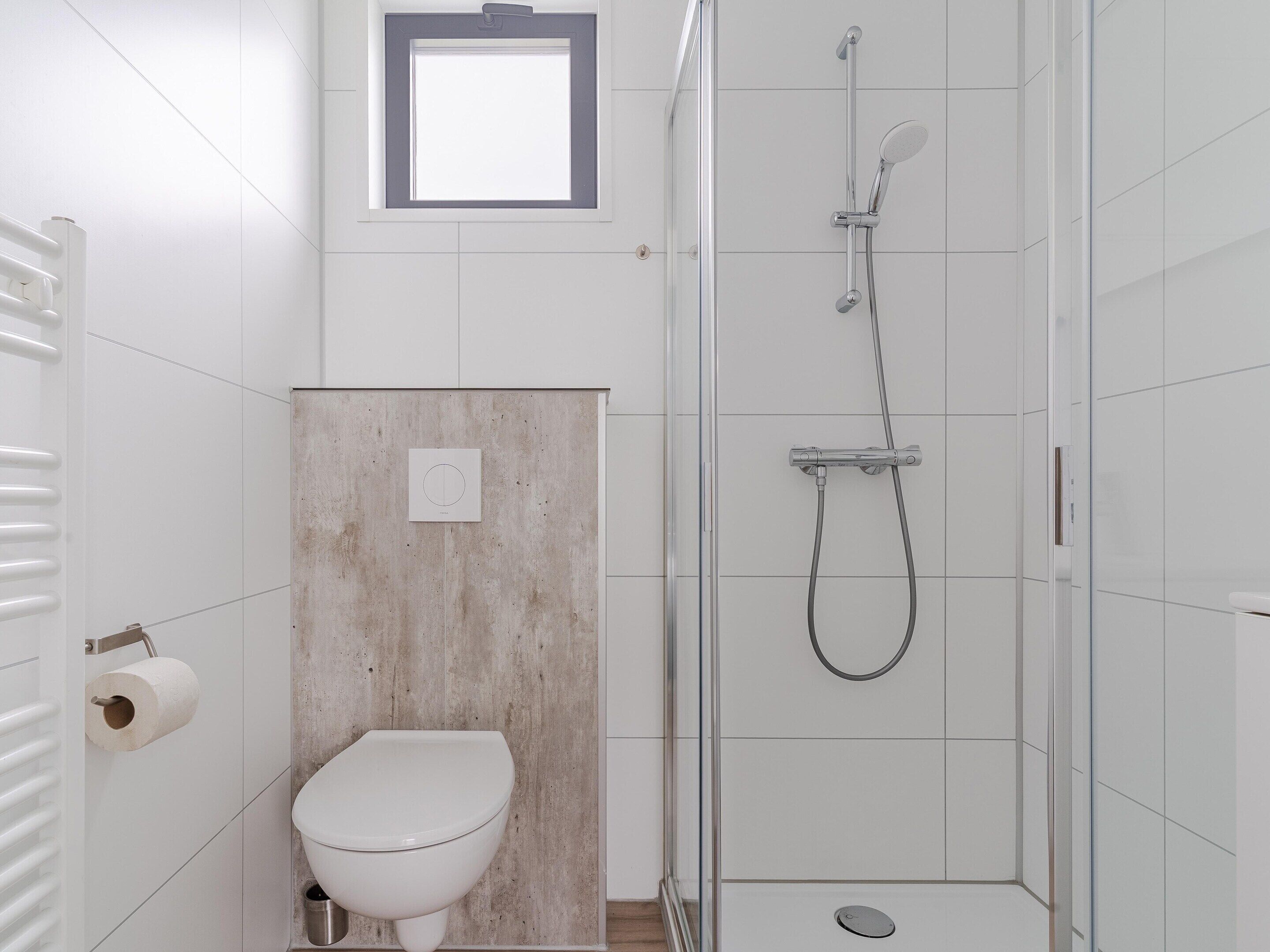 A bathroom with a toilet, a shower, and a small window.