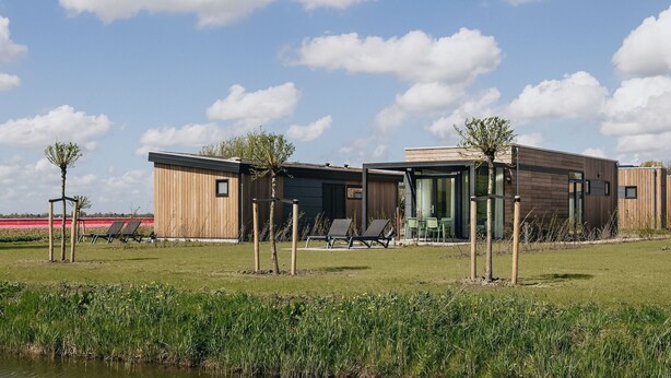 A modern building with a flat roof, wooden exterior, and a glass entrance. There are outdoor seating areas with chairs and tables. - Lodge by Markermeer With Eco-friendly Design (Wijdenes)