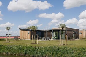 Un edificio moderno con techo plano, fachada de madera y entrada de vidrio. Hay zonas de estar al aire libre con sillas y mesas.