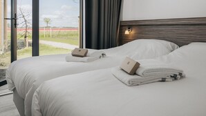 A modern hotel room with two beds, a large window with a view of a field, and a wooden headboard with a light fixture. - Lodge by Markermeer With Eco-friendly Design (Wijdenes)