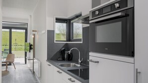 A modern kitchen with a built-in oven, a coffee maker, and a window overlooking a green landscape. - Lodge by Markermeer With Eco-friendly Design (Wijdenes)